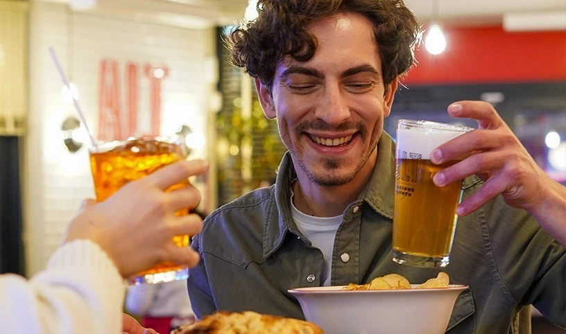 Giovane uomo con bicchiere di birra in mano degusta un aperitivo in compagnia