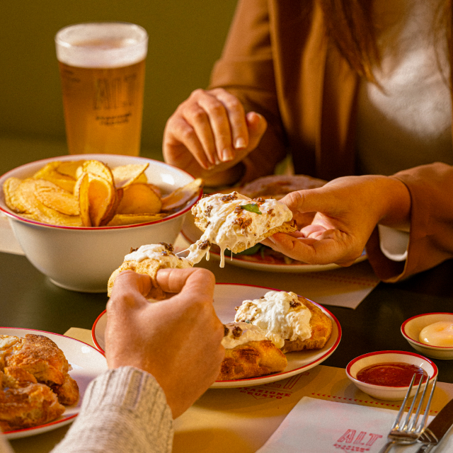 Un uomo e una donna condividono un aperitivo servito con: chips di patate con maionese e ketchup, focacce e birra alla spina